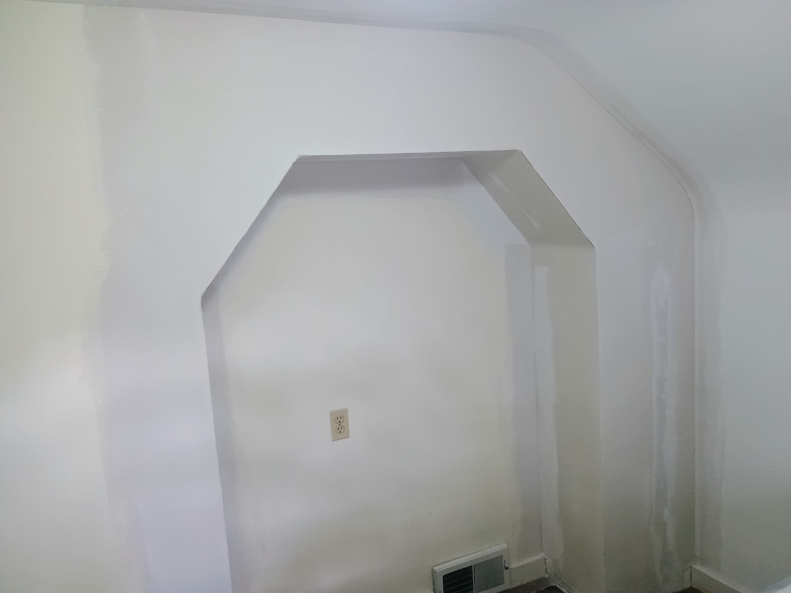 Bare mudded drywall in a sloped-ceiling bedroom with an arched alcove